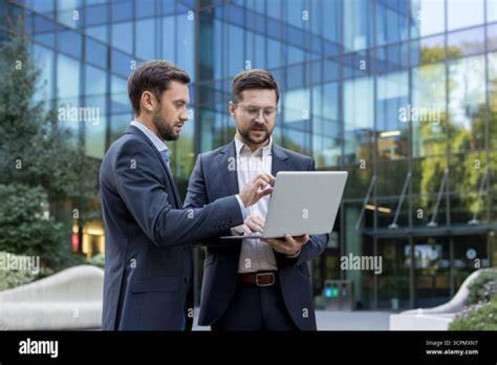 Two businessmen stand outside on golf course. Sportsmen sign paper on